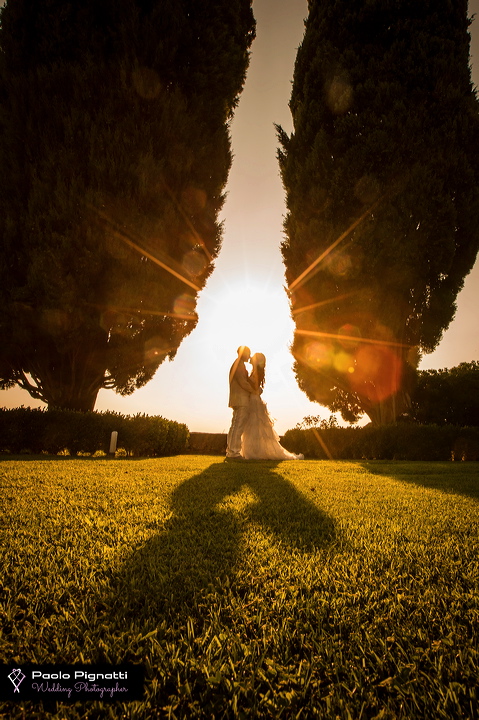 Coppia sposi che si baciano al tramonto in mezzo a due piante